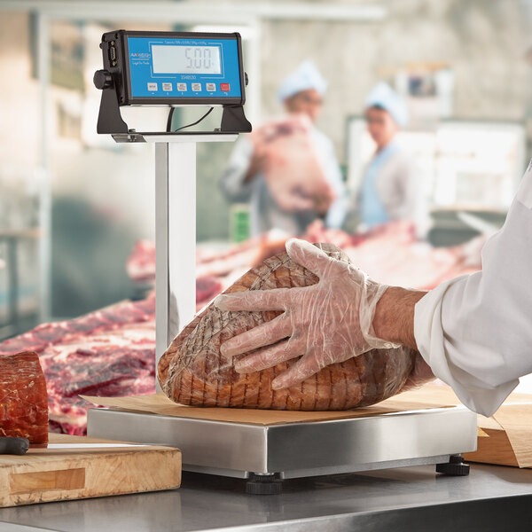 A person wearing a plastic glove weighs meat on an AvaWeigh receiving scale with a blue screen.