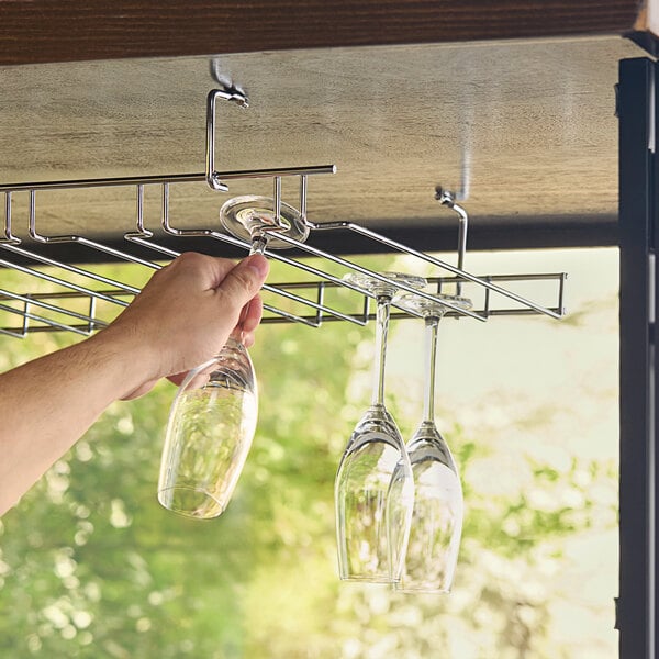 A hand holding wine glasses over a Regency chrome wire bar glass rack.