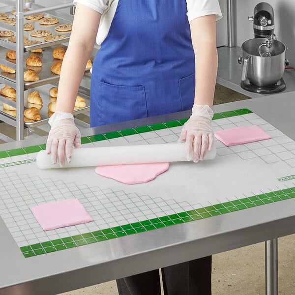 A person wearing gloves rolls out white dough on a green and white grid work mat.