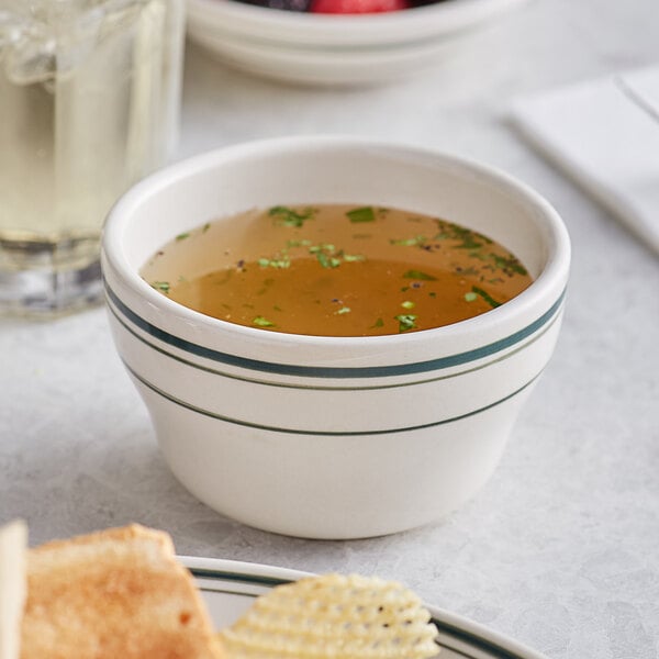 An Acopa ivory stoneware bouillon cup filled with broth on a table with food.