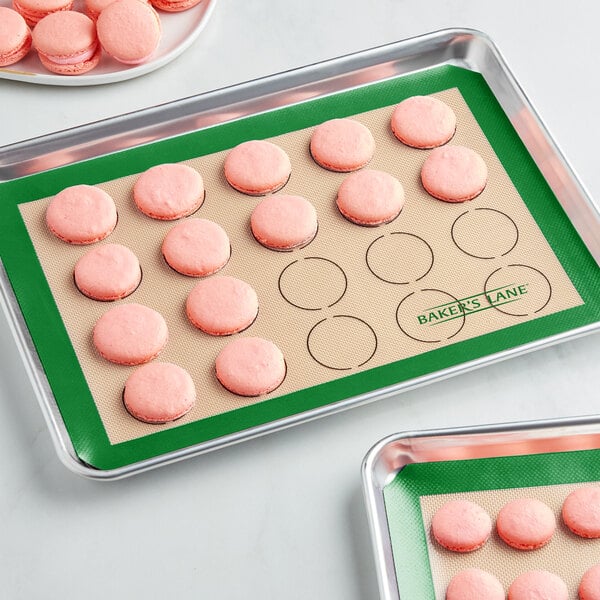 A Baker's Lane green silicone baking mat with rows of pink macarons.