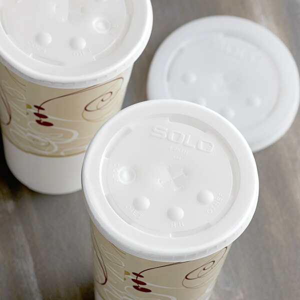 Two Solo translucent plastic lids with straw slots and identification buttons on white paper cups.