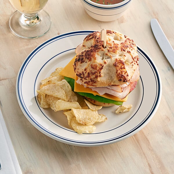 An Acopa Ivory stoneware plate with a sandwich and chips on it.