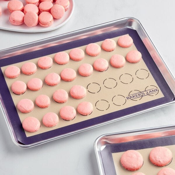 A tray of pink macarons baked with Baker's Lane purple silicone macaron baking mats on a white surface.