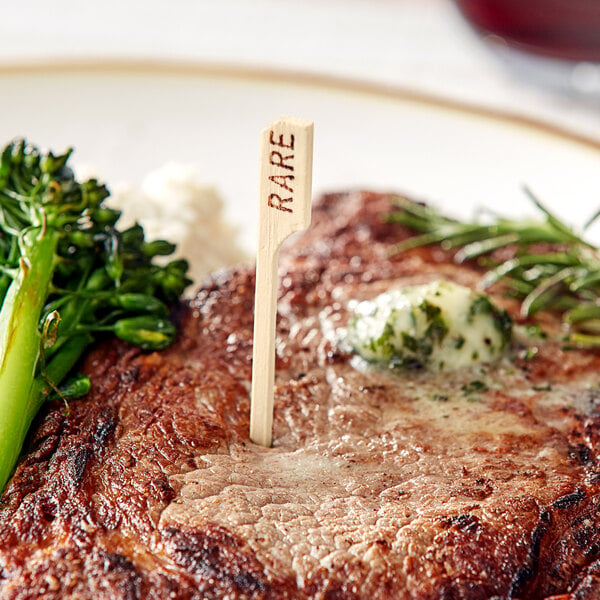 A steak with a Tablecraft bamboo meat marker on a plate with broccoli and cheese.