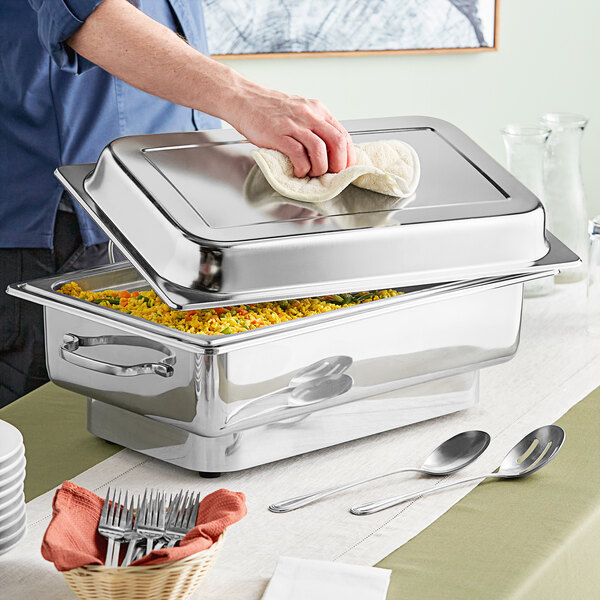 A man setting up a large stainless steel Acopa electric chafer on a table in a hotel buffet.