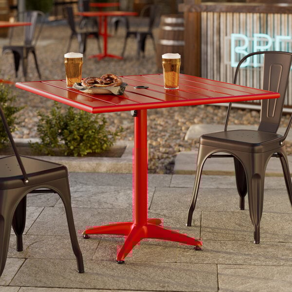 A square red powder-coated aluminum outdoor dining table with an umbrella hole, shown with drinks and food on top.
