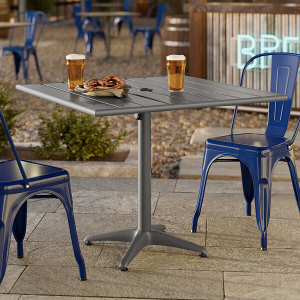 A square gray powder-coated aluminum outdoor dining table with an umbrella hole, shown with drinks and snacks on top.