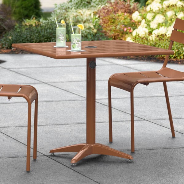 A Lancaster Table & Seating brown powder-coated aluminum table with two chairs on a patio.