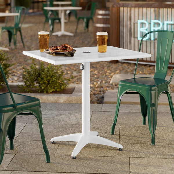 A white powder-coated aluminum outdoor dining table with an umbrella hole, shown with green chairs.