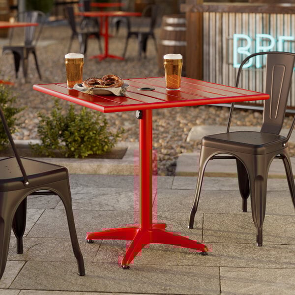 A red square aluminum outdoor dining table with an umbrella hole, shown with two metal chairs.