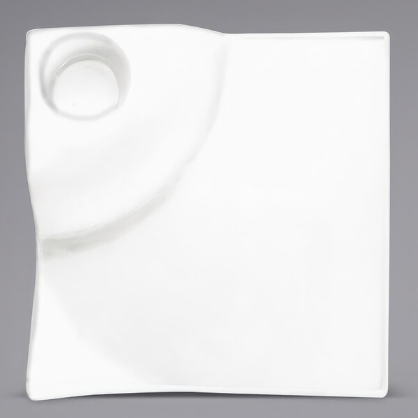 A close-up of an International Tableware bright white square porcelain plate with a circular design in the center.