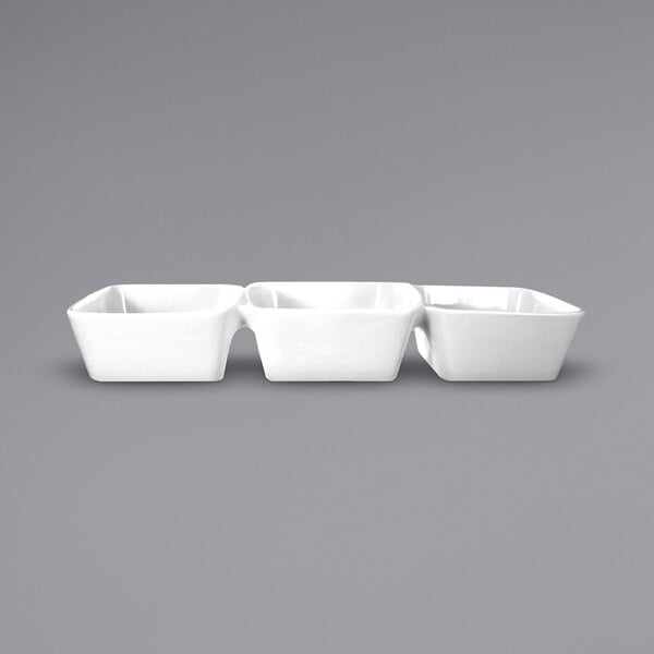 A row of three white square International Tableware Elite 3-compartment porcelain bowls.