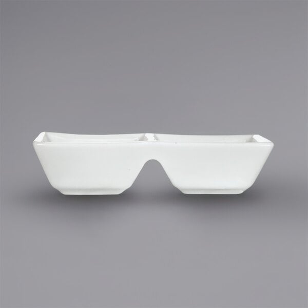 A white rectangular porcelain sauce dish with two square wells.