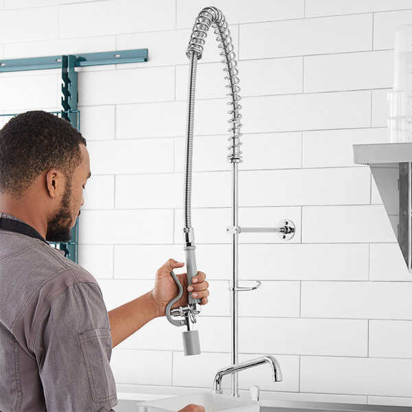 A man holding a 1.07 GPM pre-rinse spray valve assembly with a hose.
