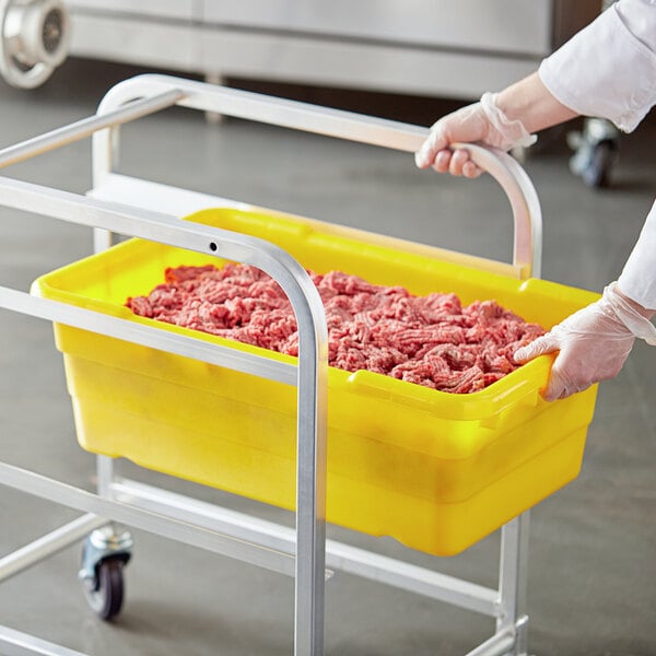 A person in gloves holding a yellow Choice meat lug full of ground meat.