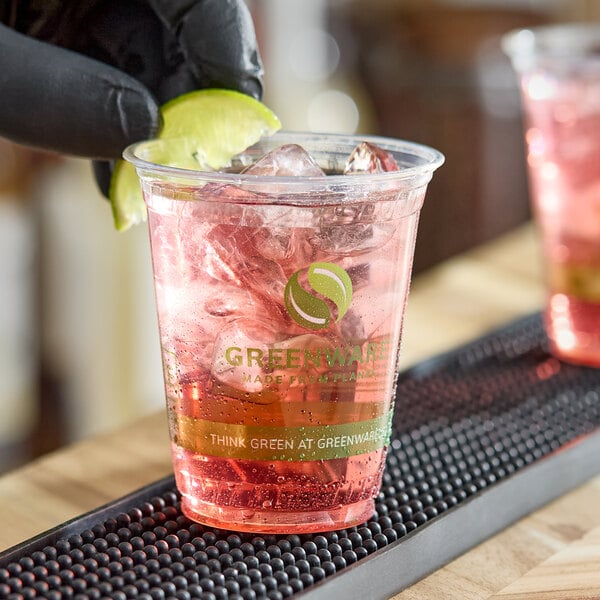 A clear 7 oz. compostable plastic cold cup with a pink beverage, ice, and a lime wedge, branded with Greenware logo and text.