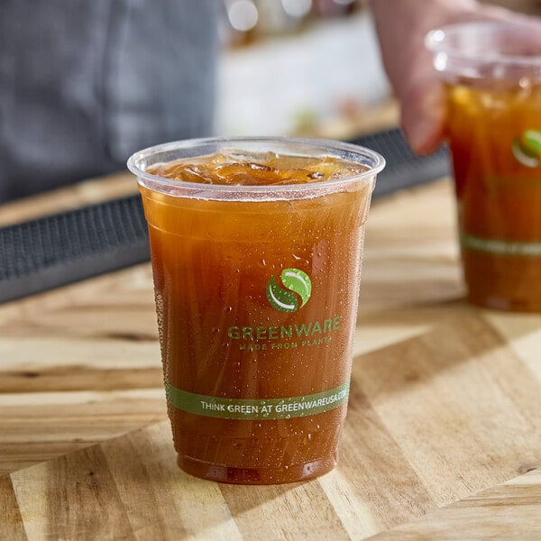 A clear compostable plastic cold cup filled with iced tea, featuring the Greenware logo and branding.