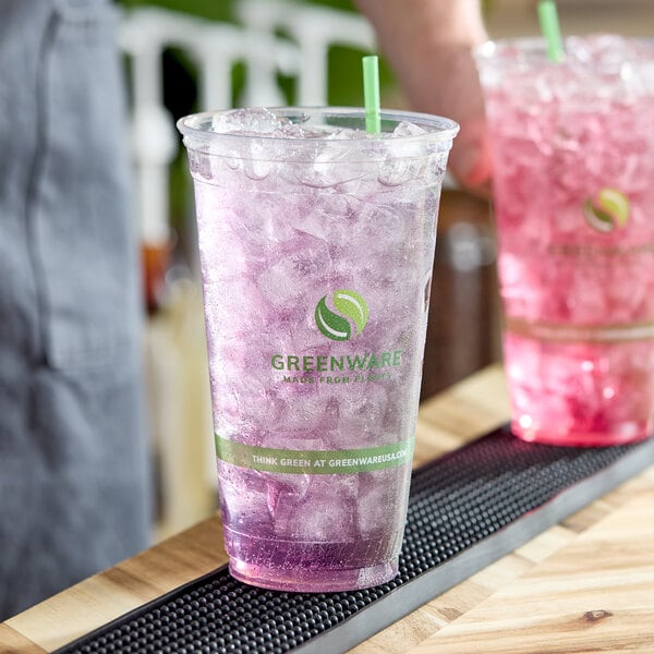 A clear 32 oz. compostable plastic cold cup filled with ice and a purple beverage, featuring Greenware branding.