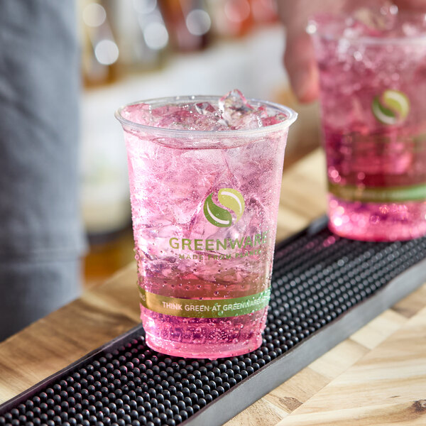 A clear 10 oz. compostable plastic cold cup filled with a pink beverage and ice, featuring Greenware branding.