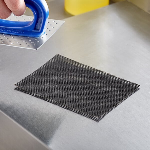 A hand using a Carlisle steel mesh grill screen to clean a metal surface.