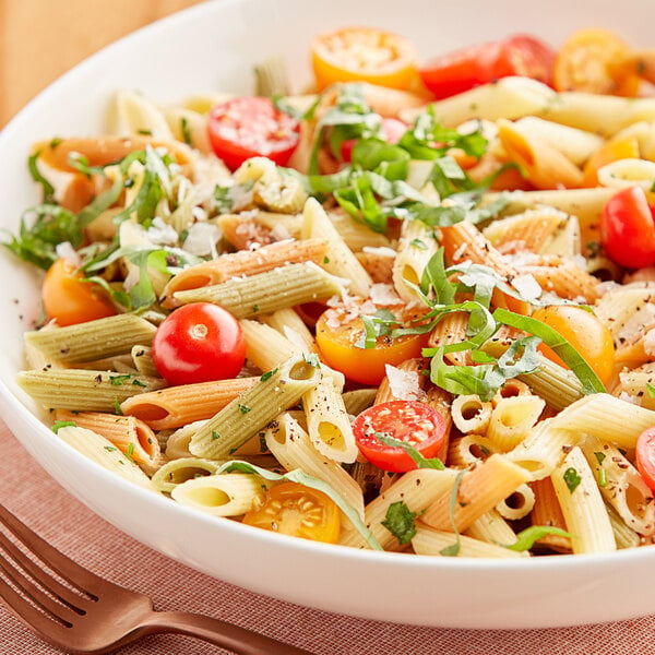 A bowl of Barilla Tri-Color Penne pasta with tomatoes, basil, and cheese.