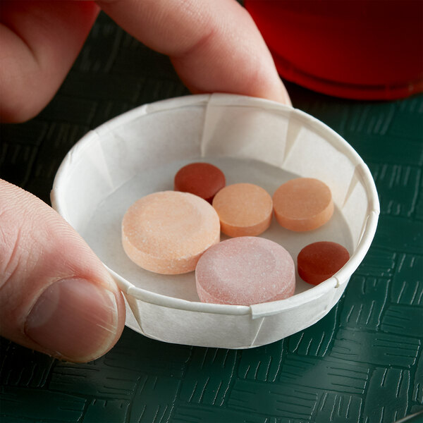 A finger holding a Genpak paper squat portion cup with pills inside.