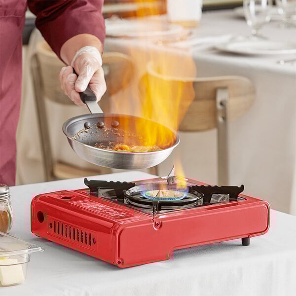 A person cooking food on a red Choice portable gas stove.