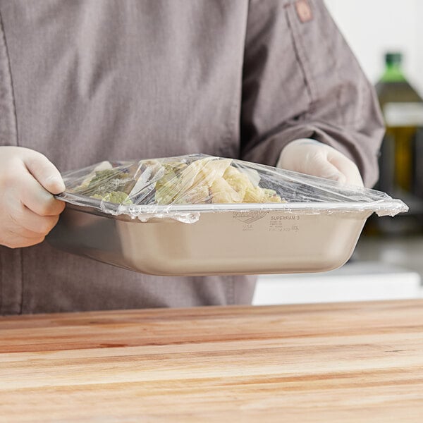 A person holding a Vollrath stainless steel steam table pan full of food.