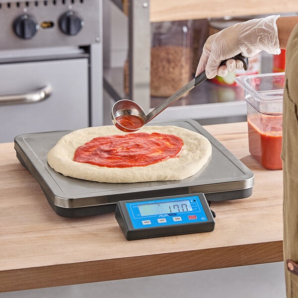 A person using a digital AvaWeigh pizza scale to measure pizza.