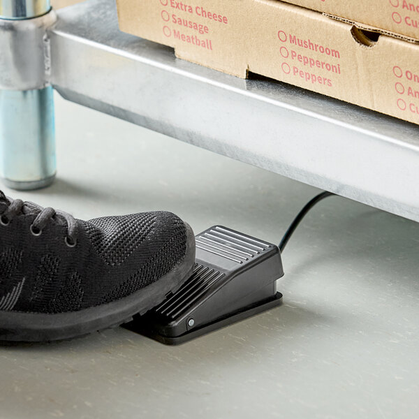 A person using the foot tare pedal to weigh pizza boxes on a table.