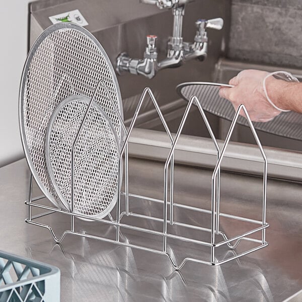 A hand holding a metal Choice four-slot pizza screen rack.