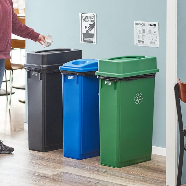 A woman standing next to a Lavex 3-stream rectangular recycle station with blue, green, and black lids.