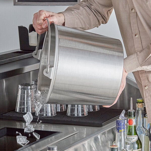 A man pouring water from a Vollrath stainless steel dairy bucket into a sink.