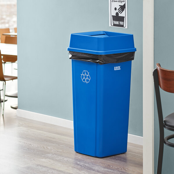 A blue Lavex square recycle bin with a black liner sitting in a room.