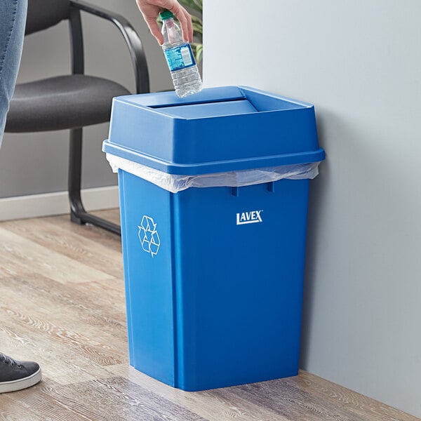 A person putting a plastic bottle into a blue Lavex recycle bin.