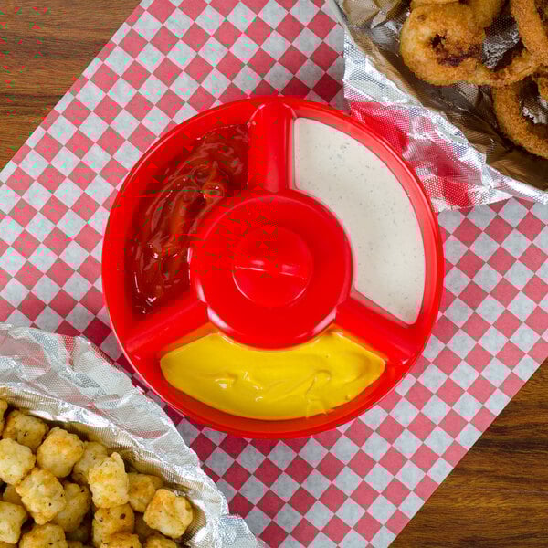 A red polypropylene container with tater tots, onion rings, and dipping sauce on a tray.
