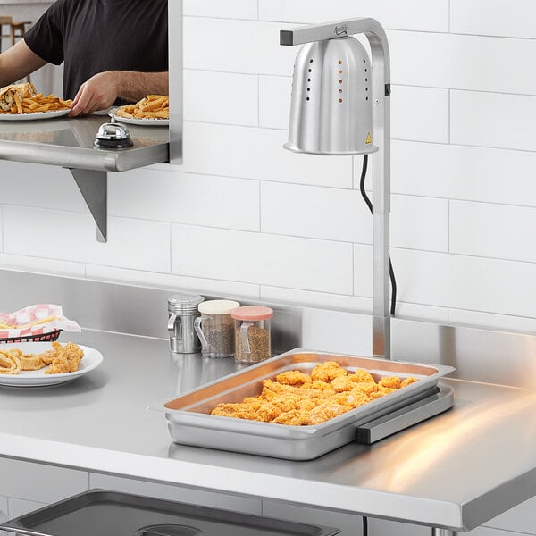 A man using an Avantco countertop heat lamp to keep food warm on a counter.