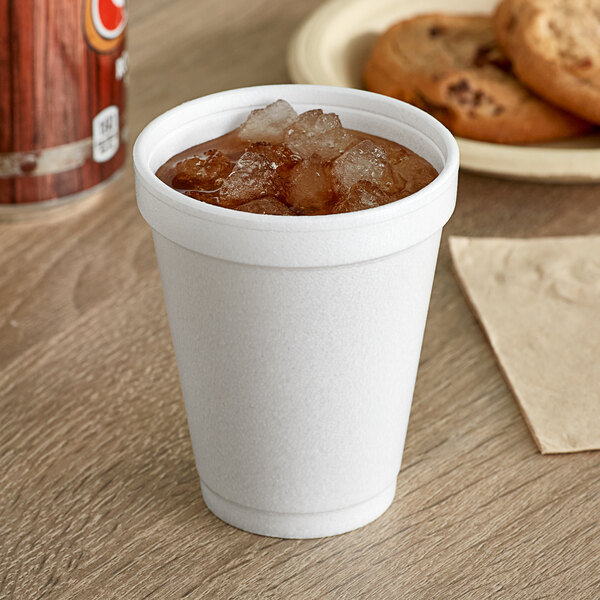 A Dart white foam cup filled with soda and ice on a table with cookies.