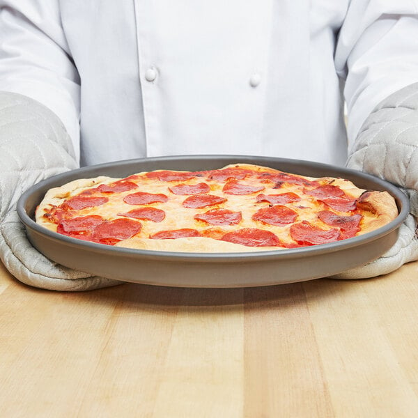 A person holding a pepperoni pizza on an American Metalcraft Hard Coat Anodized Aluminum pizza pan.