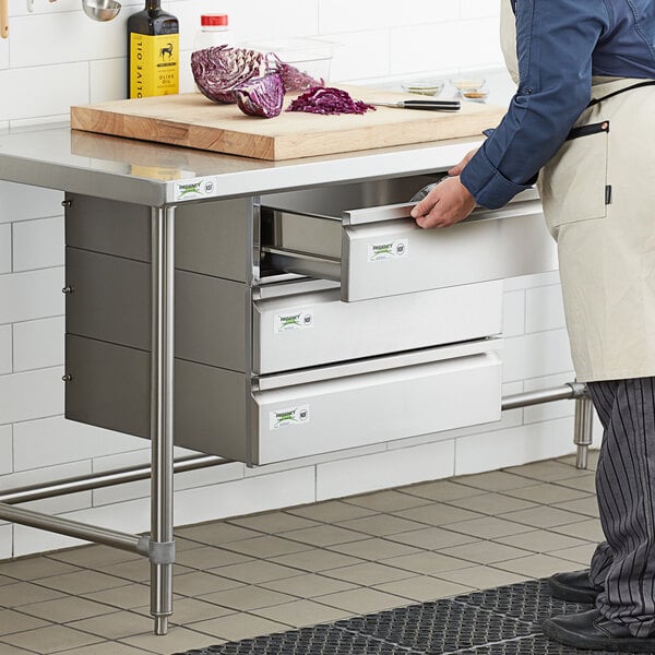 A man in a white coat using Regency stainless steel triple-stacked drawers in a kitchen.