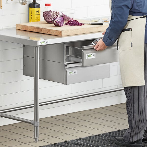 A person wearing an apron opens a Regency stainless steel drawer in a kitchen.
