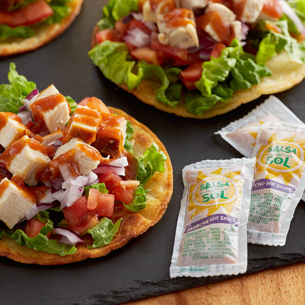 Three tacos with Salsa Del Sol sauce packets on a table.