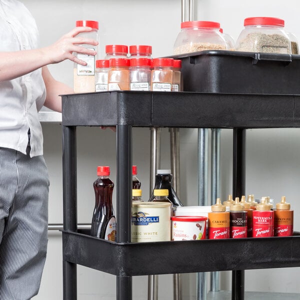 A man standing next to a black Luxor utility cart with food in plastic containers.