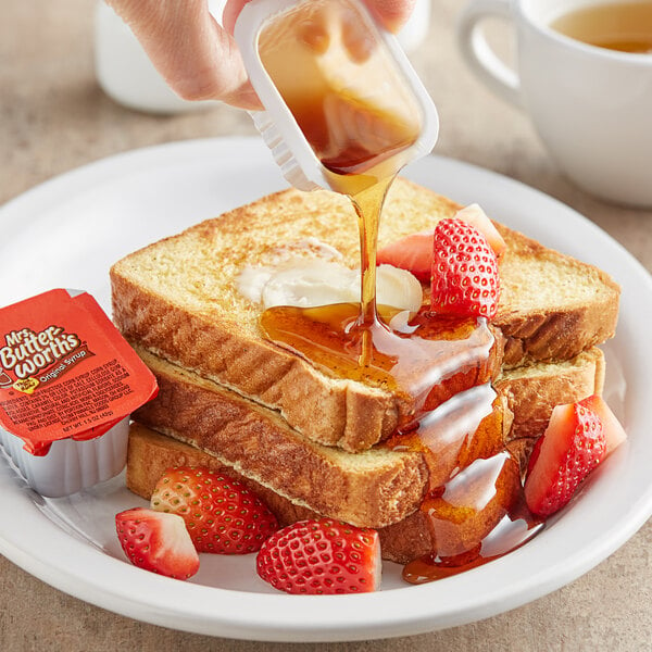 A person pouring Mrs. Buttersworth's syrup onto a stack of french toast.