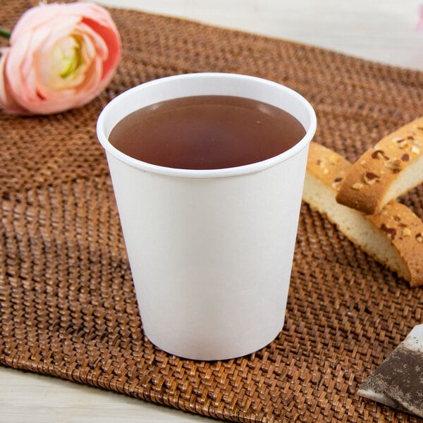 A Dart ThermoGuard white paper hot cup full of brown liquid on a table next to a pink flower.