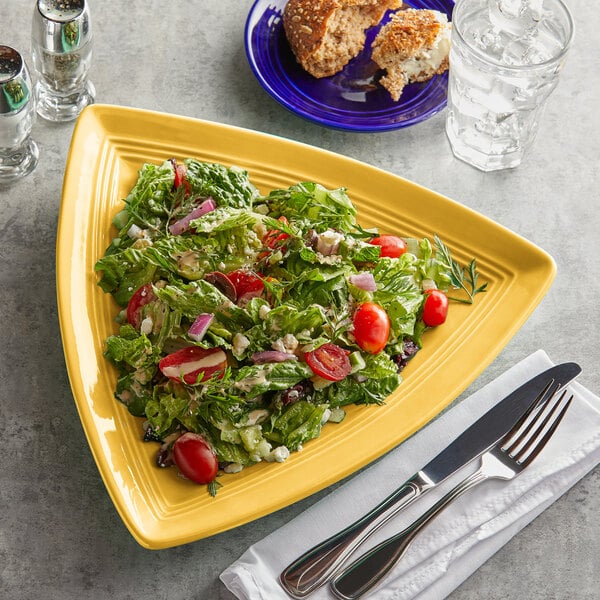 A plate of salad with tomatoes, lettuce, and other vegetables on a yellow Tuxton Concentrix china plate with a fork and knife.