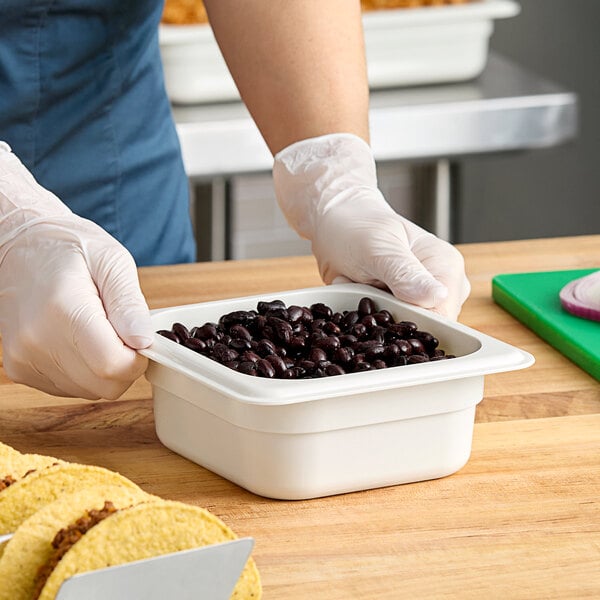A person in gloves holding a white Cambro food pan filled with black beans.