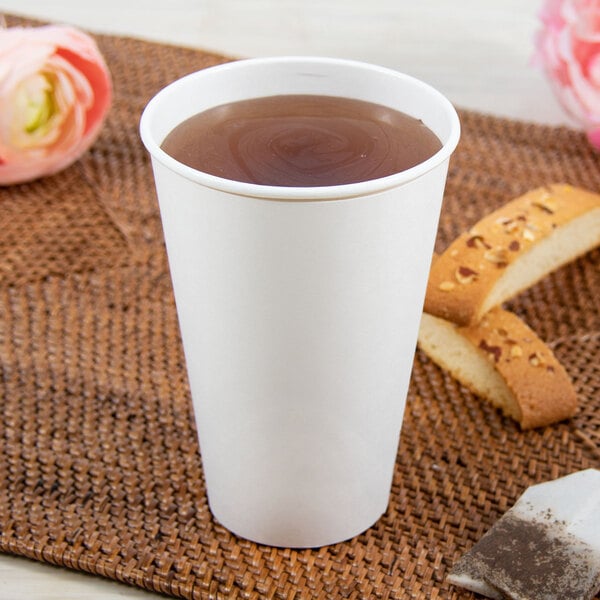 A Dart ThermoGuard white paper hot cup filled with tea on a table next to a flower.