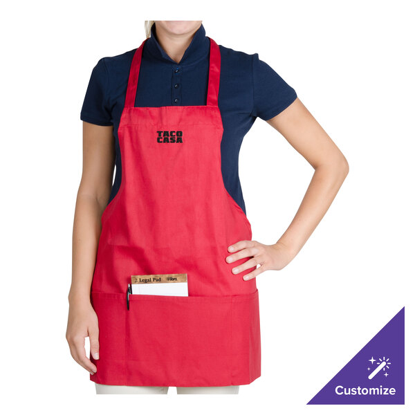 A woman wearing a red Chef Revival bib apron with a pocket on a counter in a professional kitchen.